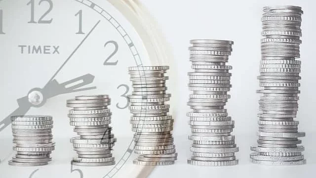 stack of coins in front of a clock