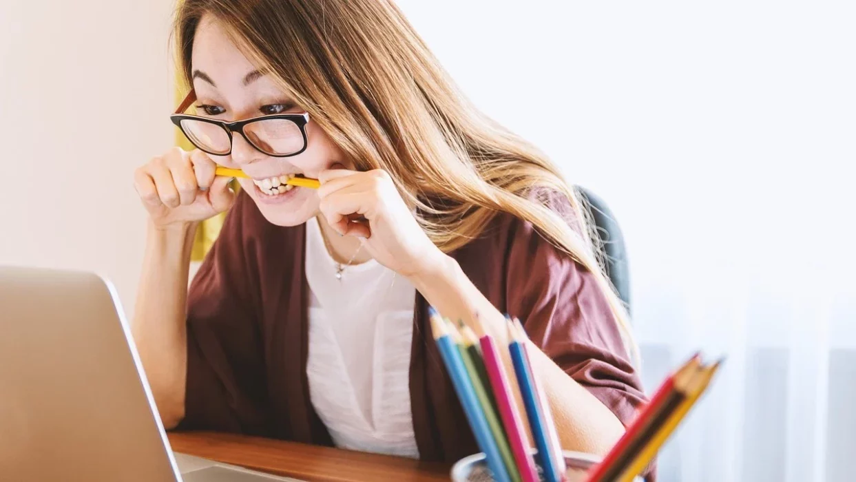 woman biting a pencil in front of a laptop